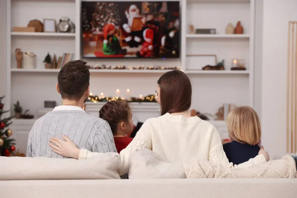Family watching Christmas movie via TV in cosy room, back view. Winter holidays atmosphere
