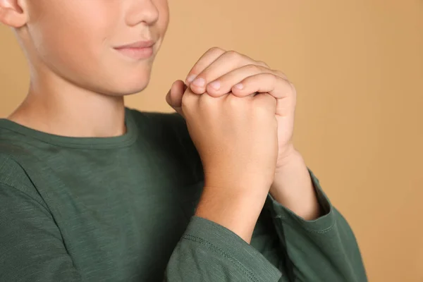 Boy with clasped hands praying on beige background, closeup