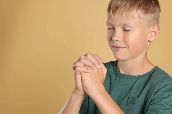 Boy with clasped hands praying on beige background, space for text