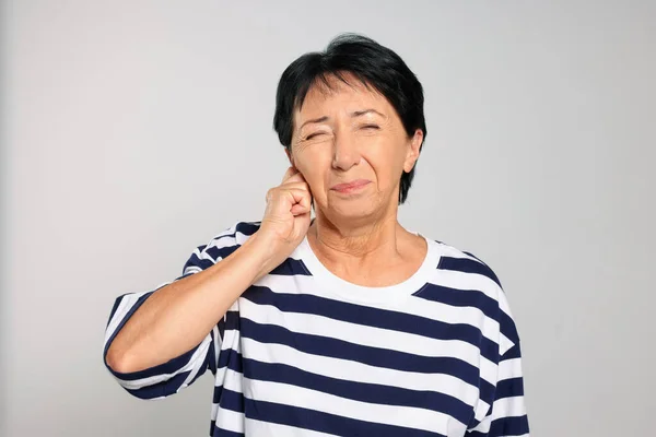 Senior woman suffering from ear pain on light grey background