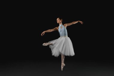 Young ballerina practicing dance moves on black background