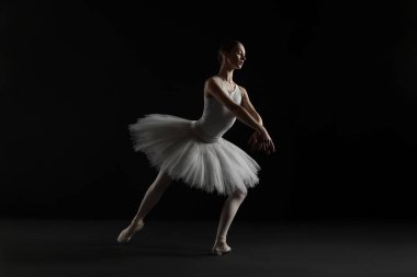 Young ballerina practicing dance moves on black background