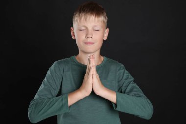 Boy with clasped hands praying on black background
