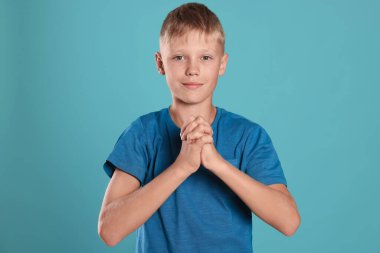 Boy with clasped hands praying on turquoise background