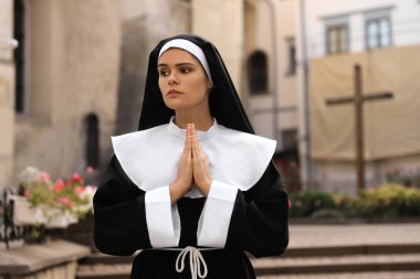 Young nun with hands clasped together praying near building outdoors