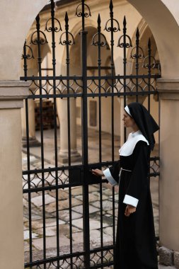 Young nun in cassock near metal door outdoors