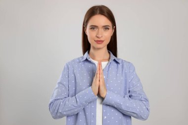 Woman with clasped hands praying on light grey background