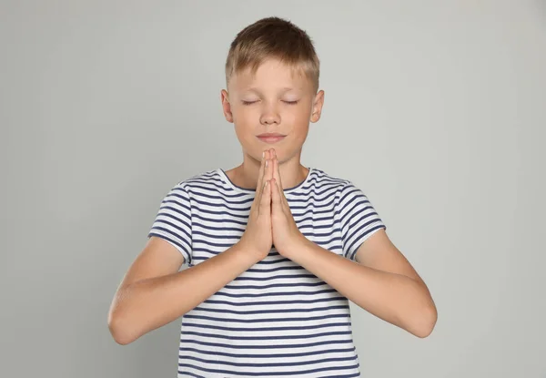Boy with clasped hands praying on light grey background