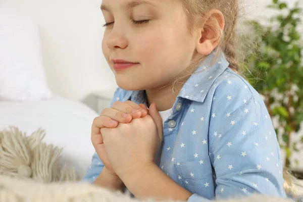 Girl with clasped hands praying near bed, closeup