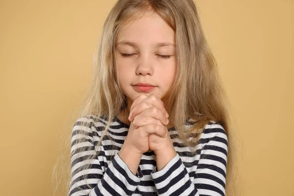 Girl with clasped hands praying on beige background