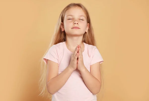 Girl with clasped hands praying on beige background