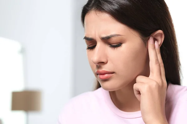 Young woman suffering from ear pain indoors, closeup. Space for text