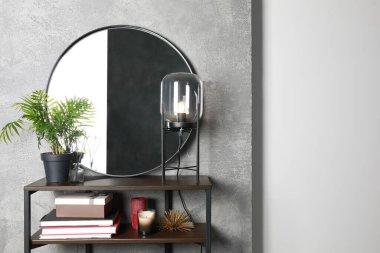 Stylish round mirror, lamp and houseplant on stand indoors. Interior design