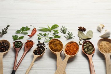 Beyaz ahşap masada farklı baharat ve otlarla dolu kaşıklar. Metin için boşluk