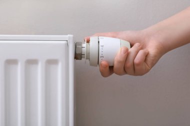 Girl adjusting heating radiator thermostat near white wall, closeup