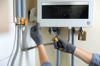Man repairing gas boiler with screwdriver indoors, closeup