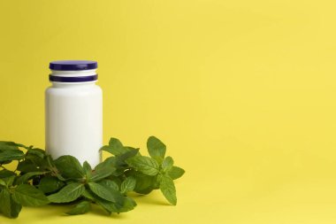 Medicine bottle near green leaves on yellow background, space for text