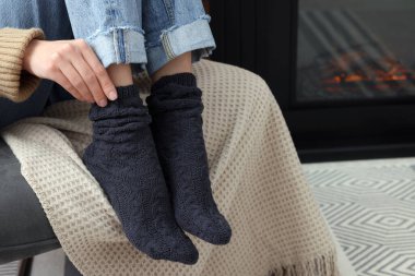 Woman in warm socks relaxing near fireplace at home, closeup