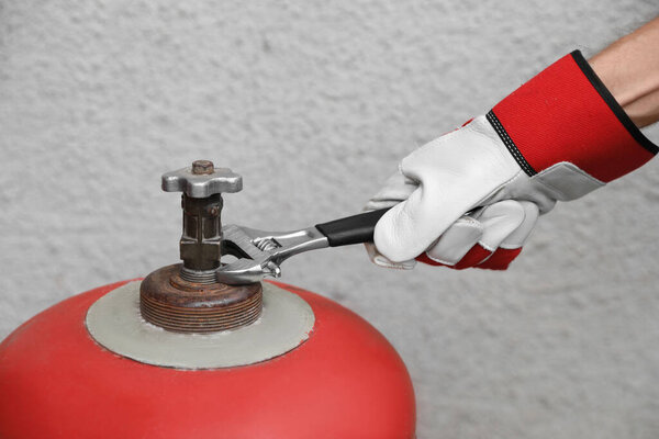 Worker with adjustable wrench opening red gas cylinder near wall, closeup