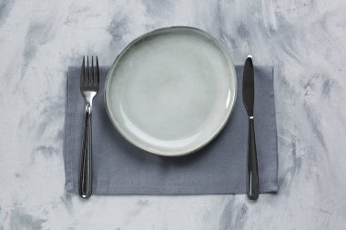 Empty plate, fork and knife on light grey table, top view