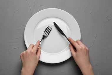 Woman with empty plate and cutlery at grey textured table, top view
