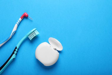 Container with dental floss and toothbrushes on light blue background, flat lay. Space for text