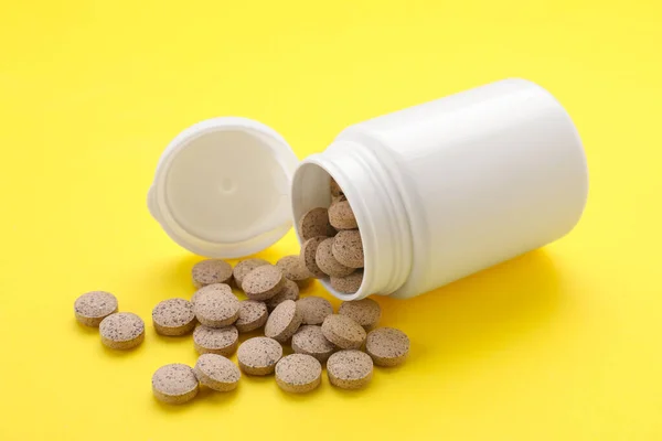 Medical bottle with beer yeast pills on yellow background, closeup