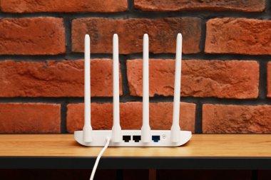 New white Wi-Fi router on wooden table near brick wall