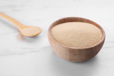Bowl and spoon with active dry yeast on white marble table, closeup