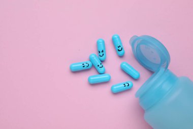 Bottle and antidepressant pills with funny faces on pink background, flat lay. Space for text