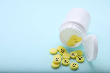 Sarı antidepresanlar, mutlu simgeler ve açık mavi arka planda tıbbi şişeler, yakın plan. Metin için boşluk