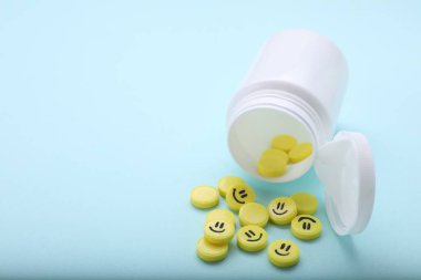 Yellow antidepressants with happy emoticons and medical bottle on light blue background, closeup. Space for text clipart