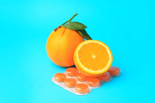 Blisters with cough drops and fresh oranges on light blue background