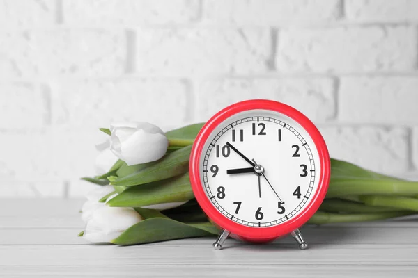 Red Alarm Clock Beautiful Tulips White Wooden Table Brick Wall — Stok fotoğraf