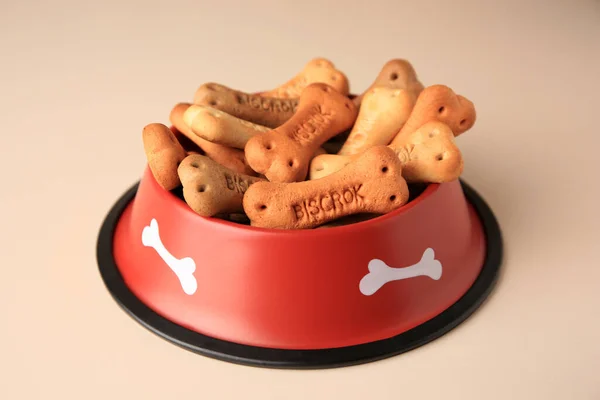 Bone shaped dog cookies in feeding bowl on beige table, closeup