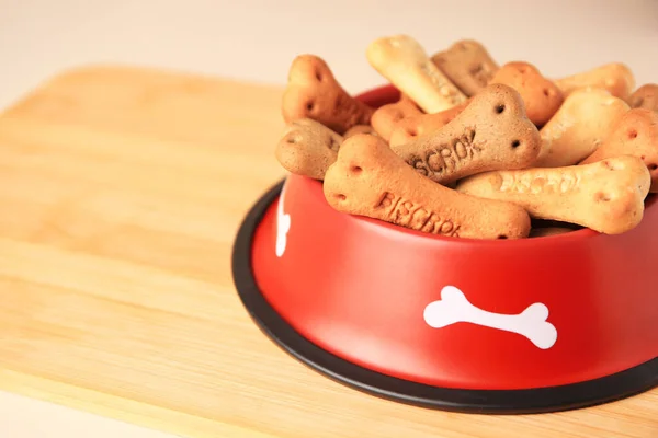 Bone shaped dog cookies in feeding bowl on wooden table, closeup. Space for text