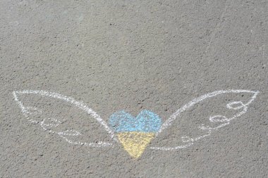 Heart and wings drawn with blue and yellow chalks on asphalt outdoors, top view. Space for text