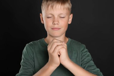 Boy with clasped hands praying on black background