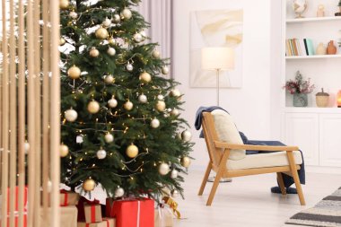 Beautiful Christmas tree with festive lights, gifts and armchair in living room. Interior design