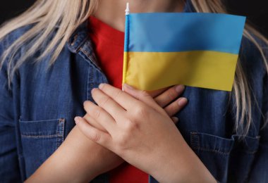 Woman holding Ukrainian flag on black background, closeup