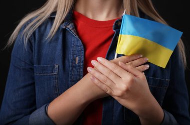 Woman holding Ukrainian flag on black background, closeup