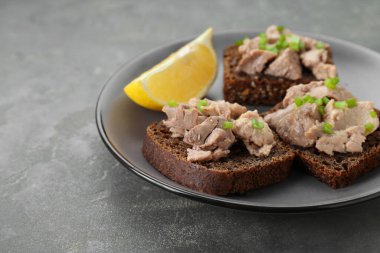 Tasty sandwiches with cod liver, lemon and green onion on light grey table