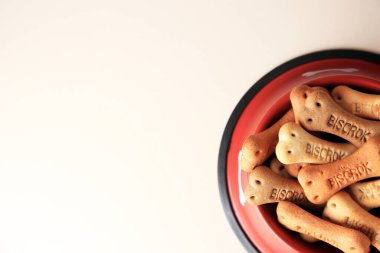 Bone shaped dog cookies in feeding bowl on beige table, top view. Space for text