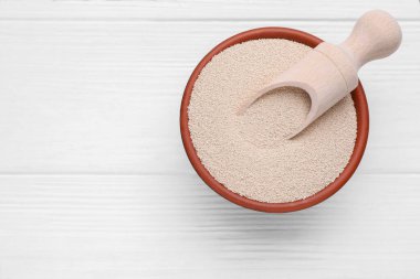 Bowl and scoop with active dry yeast on white wooden table, top view. Space for text
