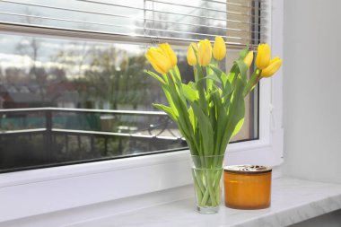 Wonderful tulips and candle on window sill indoors, space for text. Spring atmosphere
