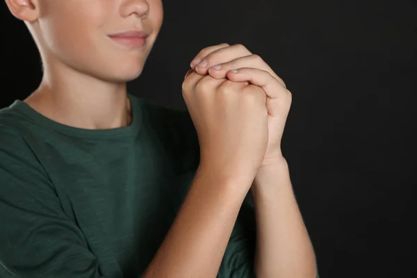 Boy with clasped hands praying on black background, closeup