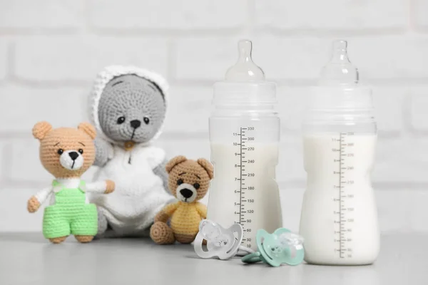 Feeding bottles with milk, pacifiers and crochet toys on light grey table