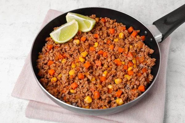Fried minced meat, carrot, corn and lime in pan on white textured table