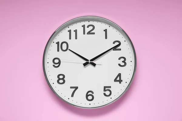 Stylish round clock on pale pink background, top view. Interior element