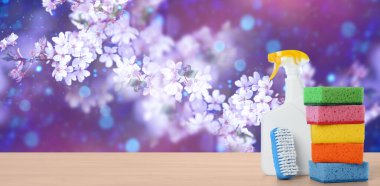 Spring cleaning. Detergents and tools on wooden surface against blossoming tree, space for text. Banner design clipart
